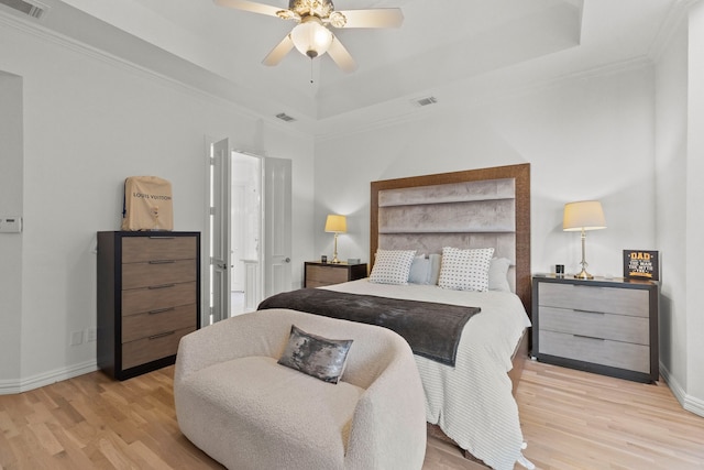 bedroom featuring light wood-style floors, a tray ceiling, visible vents, and baseboards