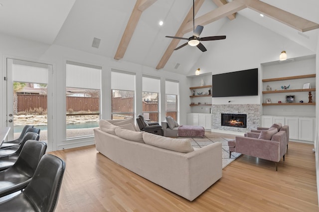 living room featuring a stone fireplace, light wood finished floors, beam ceiling, and a healthy amount of sunlight