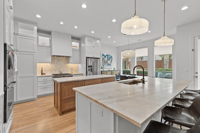 kitchen featuring custom exhaust hood, stainless steel appliances, tasteful backsplash, a sink, and an island with sink