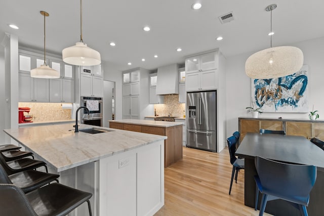 kitchen featuring visible vents, light wood-style flooring, stainless steel appliances, a large island with sink, and a sink