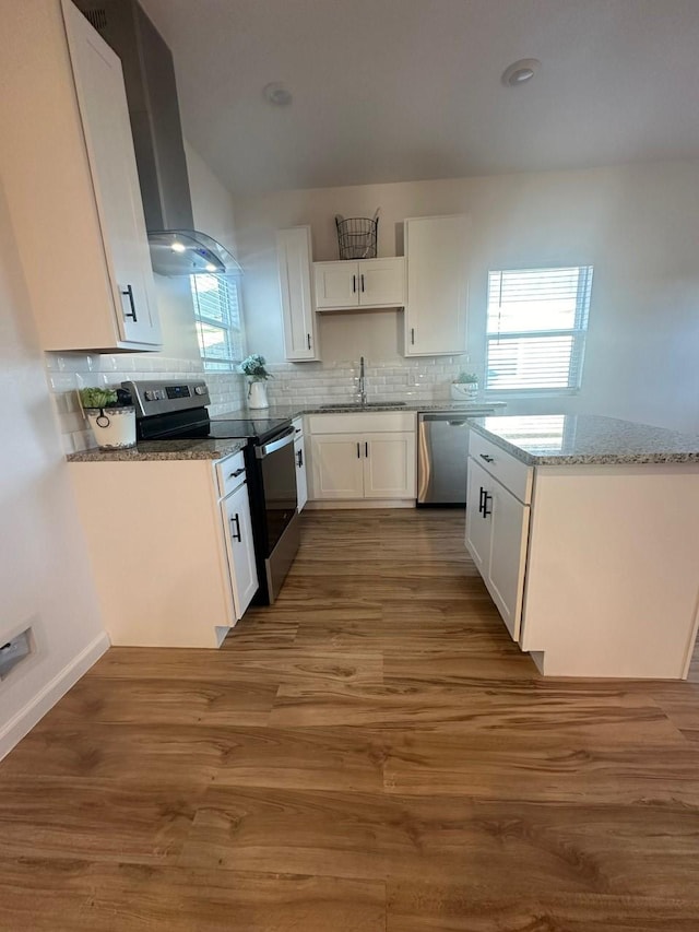 kitchen with white cabinets, appliances with stainless steel finishes, wood finished floors, light stone countertops, and a sink