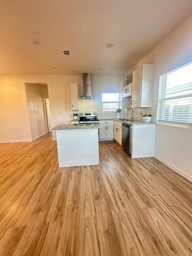 kitchen featuring visible vents, wall chimney range hood, light wood-type flooring, and appliances with stainless steel finishes