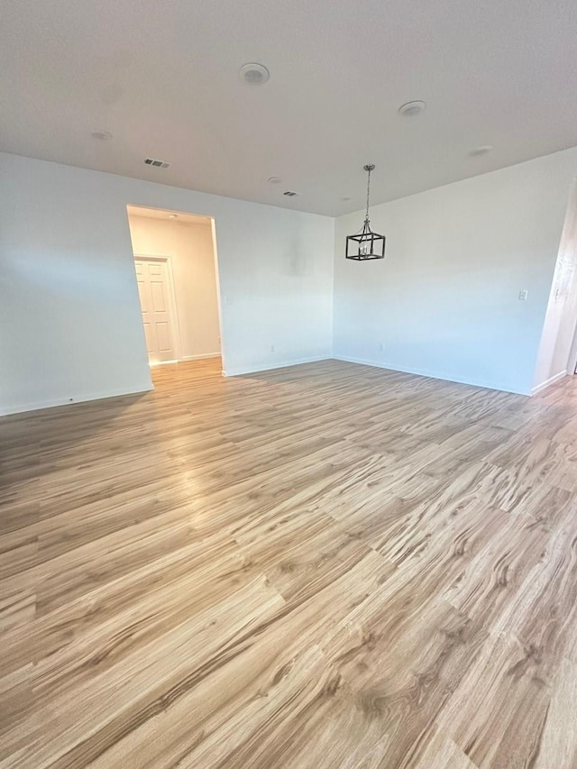 spare room with light wood-type flooring, visible vents, and baseboards