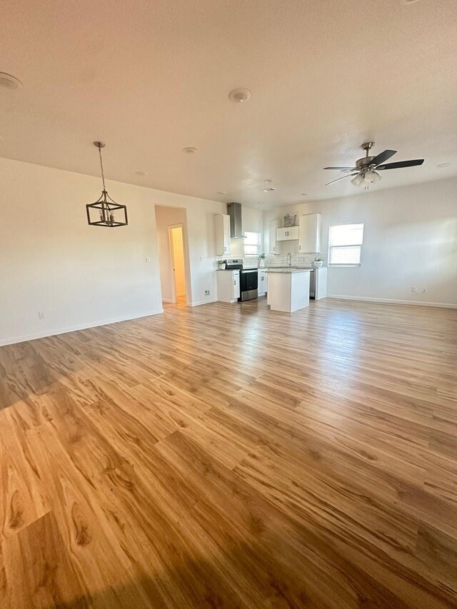 unfurnished living room featuring ceiling fan, light wood finished floors, and baseboards