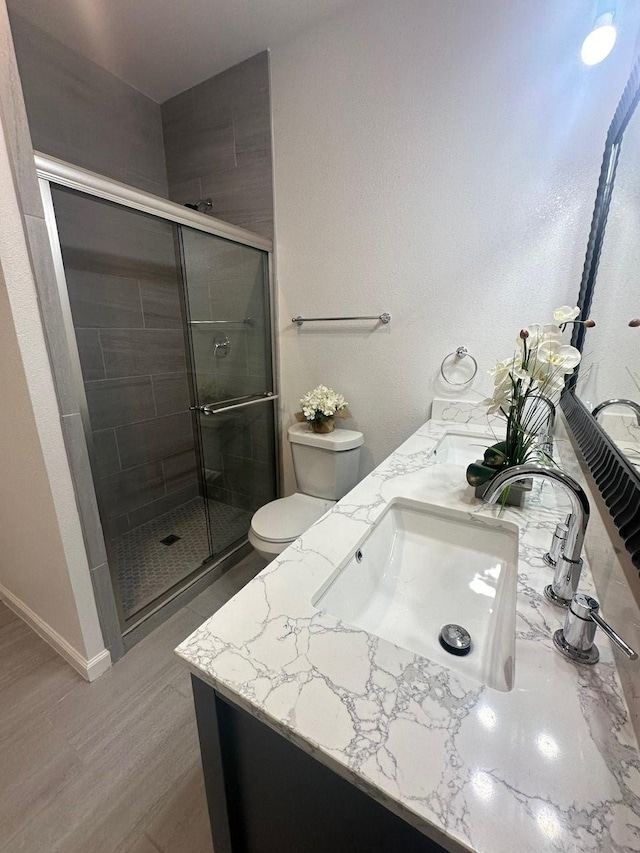 bathroom with toilet, a stall shower, vanity, wood finished floors, and baseboards