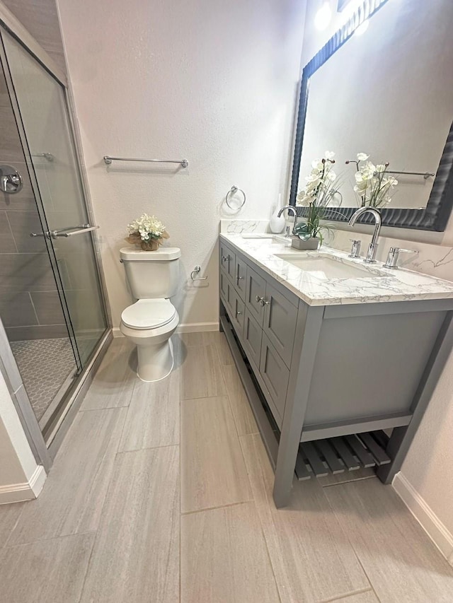 bathroom featuring toilet, a stall shower, baseboards, and a sink