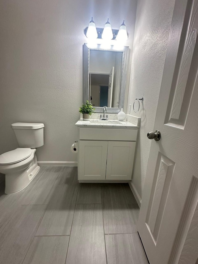 half bathroom with a textured wall, vanity, toilet, and baseboards