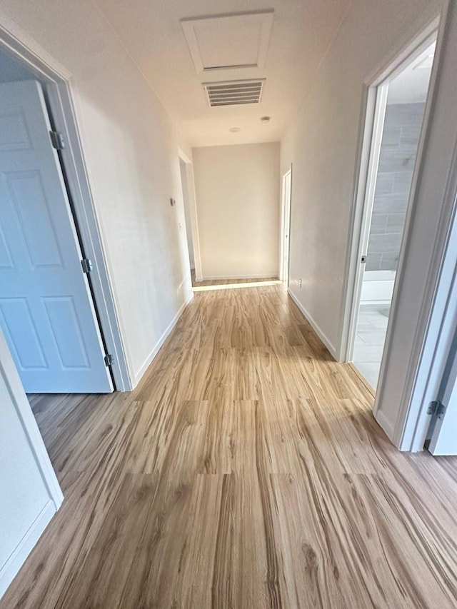 hall featuring baseboards, attic access, visible vents, and wood finished floors