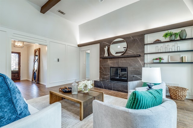 living area with visible vents, a decorative wall, a premium fireplace, wood finished floors, and beamed ceiling