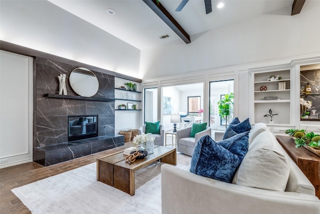 living room featuring visible vents, a ceiling fan, a high end fireplace, wood finished floors, and beamed ceiling