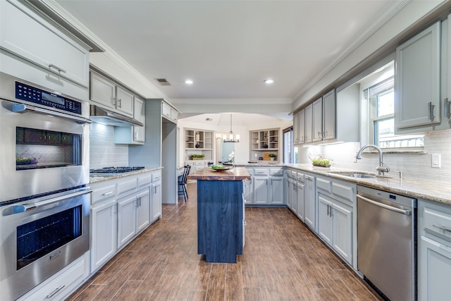 kitchen with appliances with stainless steel finishes, a sink, ornamental molding, and wooden counters