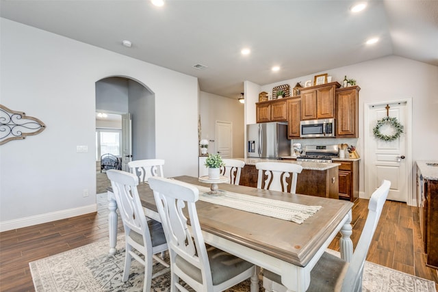 dining space featuring baseboards, visible vents, arched walkways, dark wood-type flooring, and vaulted ceiling