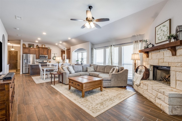 living room featuring visible vents, a ceiling fan, dark wood-style floors, vaulted ceiling, and a fireplace