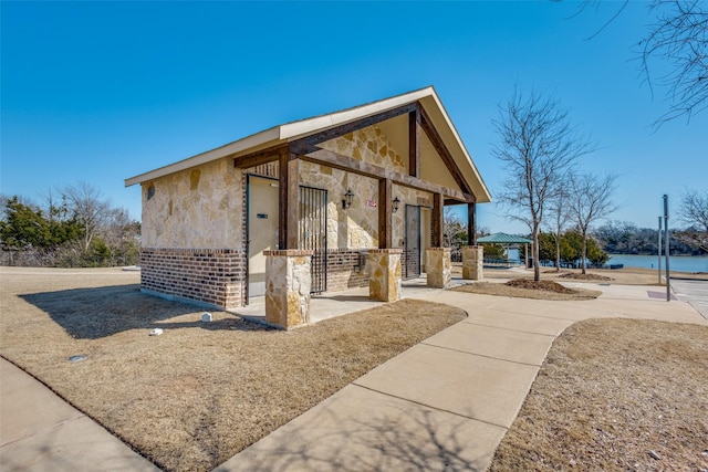 view of side of property featuring stone siding, brick siding, a water view, and a gazebo