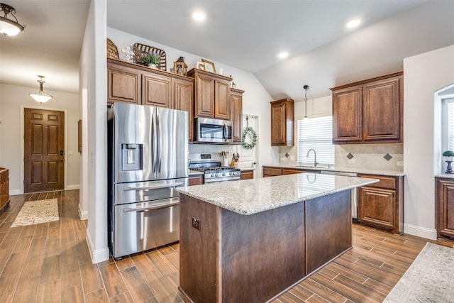 kitchen with lofted ceiling, light stone counters, stainless steel appliances, wood finish floors, and backsplash