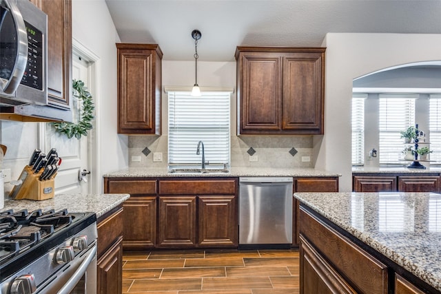 kitchen featuring wood finish floors, stainless steel appliances, tasteful backsplash, hanging light fixtures, and a sink