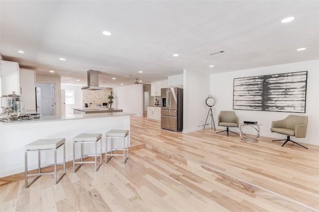 kitchen with stainless steel fridge, visible vents, white cabinets, a peninsula, and island exhaust hood