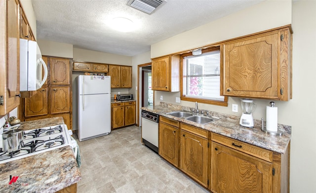 kitchen with white appliances, a sink, visible vents, light countertops, and brown cabinets