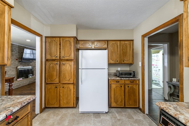 kitchen with freestanding refrigerator, brown cabinets, and a textured ceiling