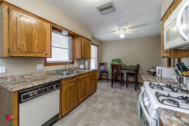 kitchen featuring brown cabinetry, white appliances, visible vents, and a sink