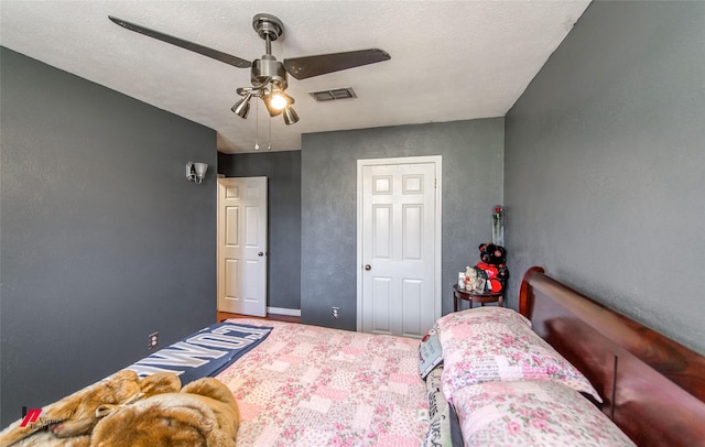 bedroom with ceiling fan, visible vents, and a textured wall