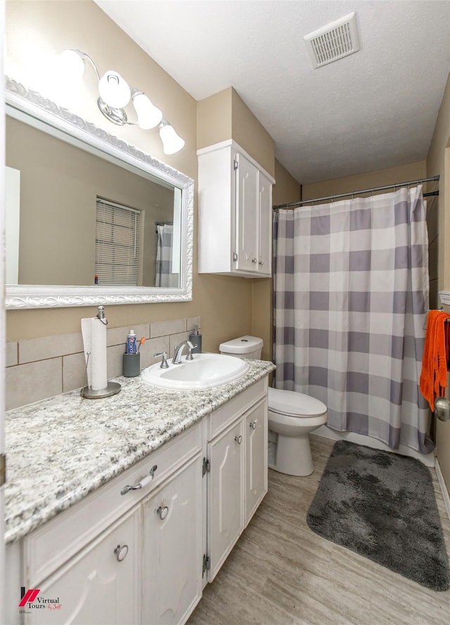 full bath with a textured ceiling, toilet, wood finished floors, vanity, and visible vents