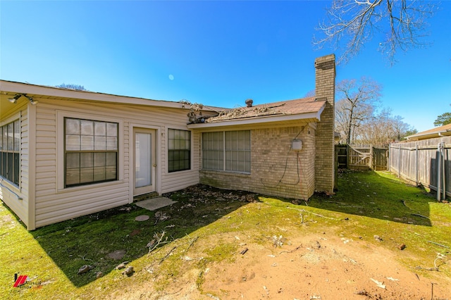 back of house featuring brick siding, fence, a chimney, and a lawn