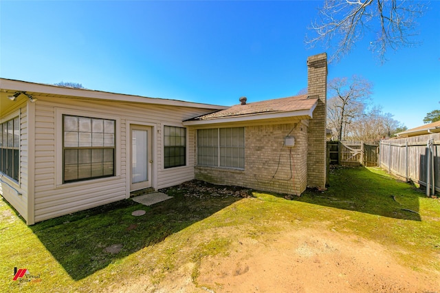 back of house featuring a yard, a chimney, fence, and brick siding