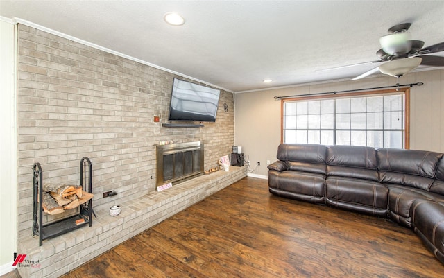 living area featuring dark wood-style floors, a fireplace, a ceiling fan, ornamental molding, and a textured ceiling