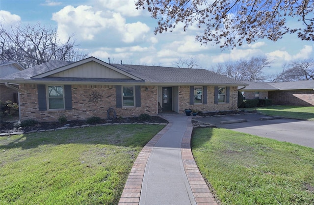 single story home featuring a shingled roof, a front yard, and brick siding