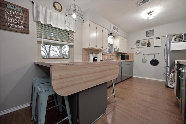 kitchen featuring visible vents, white cabinets, decorative backsplash, a breakfast bar area, and dark wood-style flooring