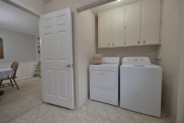 washroom featuring a decorative wall, wainscoting, cabinet space, washer and clothes dryer, and crown molding