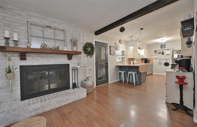 living room featuring a fireplace, a textured ceiling, wood finished floors, beamed ceiling, and baseboards