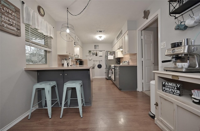 kitchen featuring dark wood-style floors, a peninsula, stainless steel appliances, a kitchen bar, and backsplash