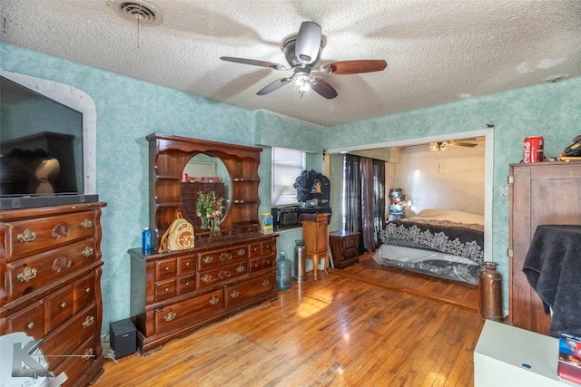 bedroom with ceiling fan, a textured ceiling, visible vents, and hardwood / wood-style floors