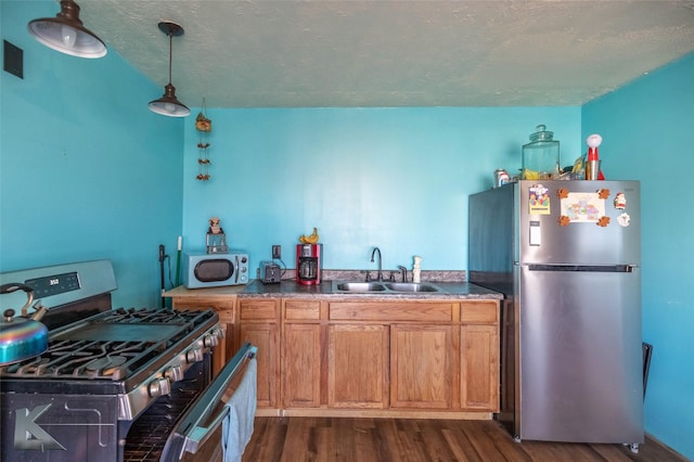 kitchen with dark wood finished floors, appliances with stainless steel finishes, brown cabinets, pendant lighting, and a sink