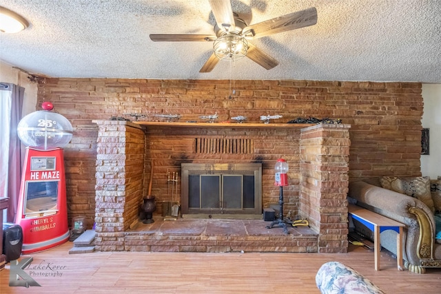 unfurnished living room featuring a textured ceiling, ceiling fan, a brick fireplace, and wood finished floors