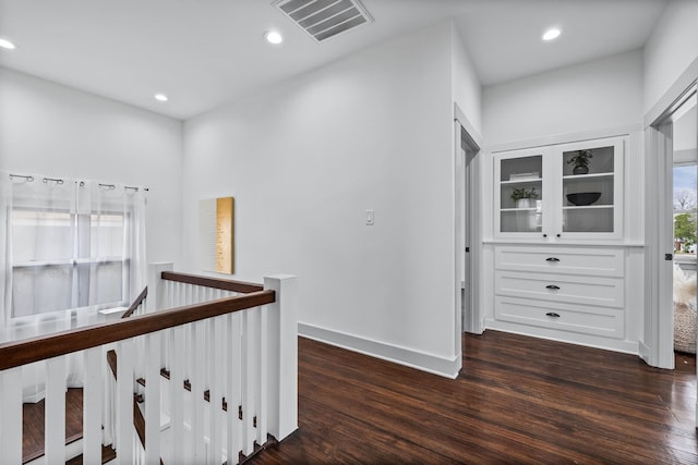 hall with dark wood-style floors, recessed lighting, visible vents, and an upstairs landing