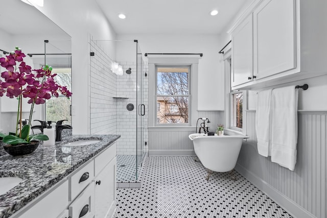 bathroom with double vanity, a stall shower, a wainscoted wall, a freestanding tub, and a sink