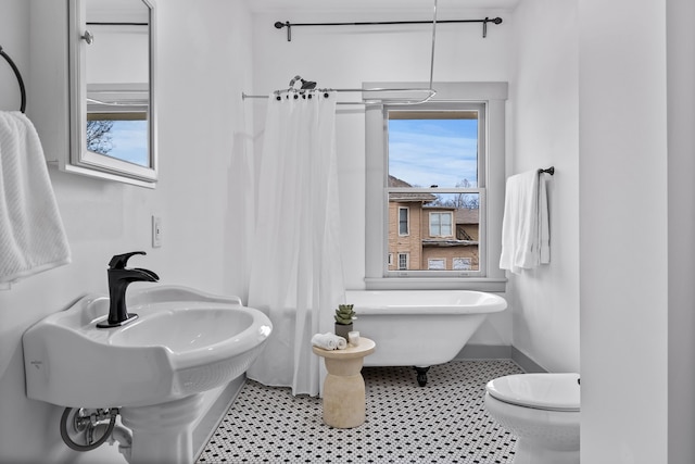 full bathroom featuring a freestanding bath, toilet, and baseboards