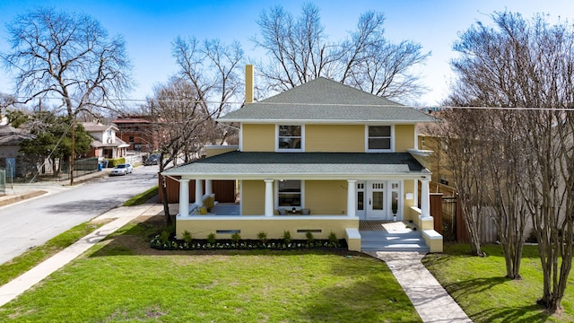 view of front facade with covered porch, french doors, roof with shingles, and a front yard