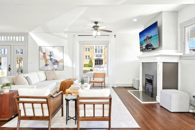 living room with a fireplace with raised hearth, ceiling fan, baseboards, and dark wood finished floors