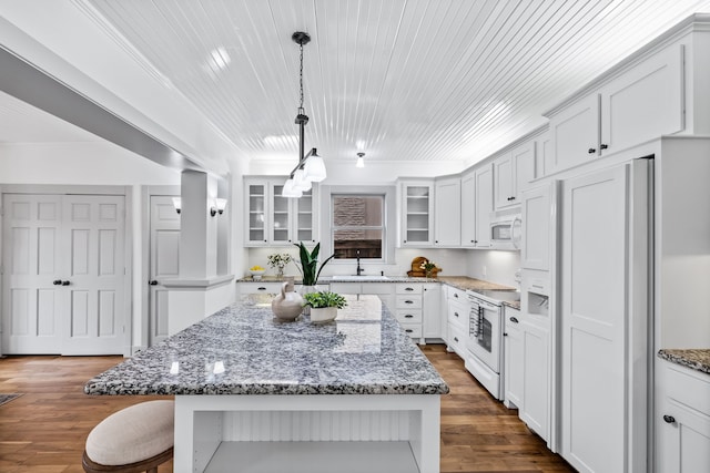 kitchen featuring white appliances, glass insert cabinets, a breakfast bar, a center island, and a sink