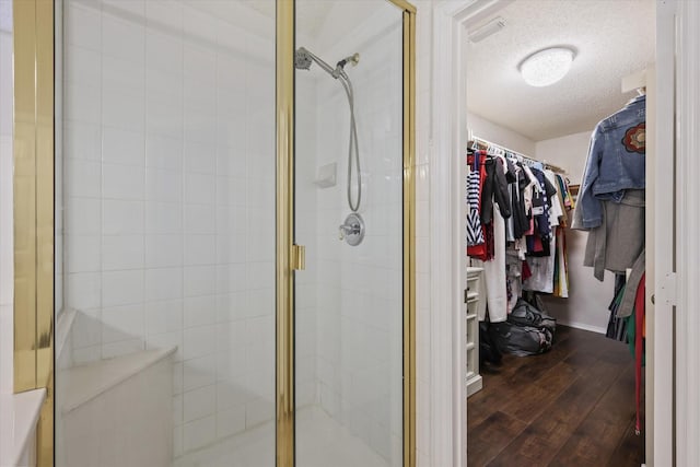 bathroom featuring a stall shower, a spacious closet, a textured ceiling, and wood finished floors