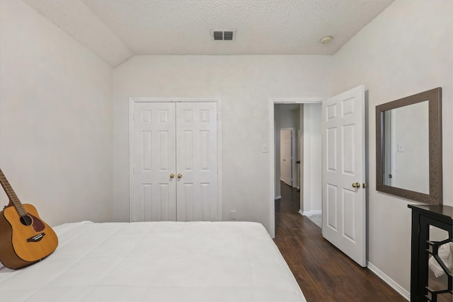 bedroom featuring a closet, visible vents, dark wood-type flooring, a textured ceiling, and baseboards