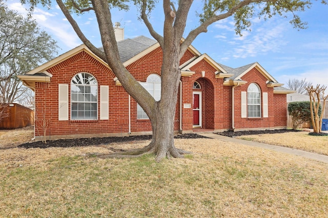 view of front facade featuring brick siding, a shingled roof, a chimney, and a front yard