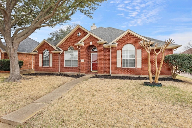 ranch-style home with brick siding, roof with shingles, a chimney, and a front yard