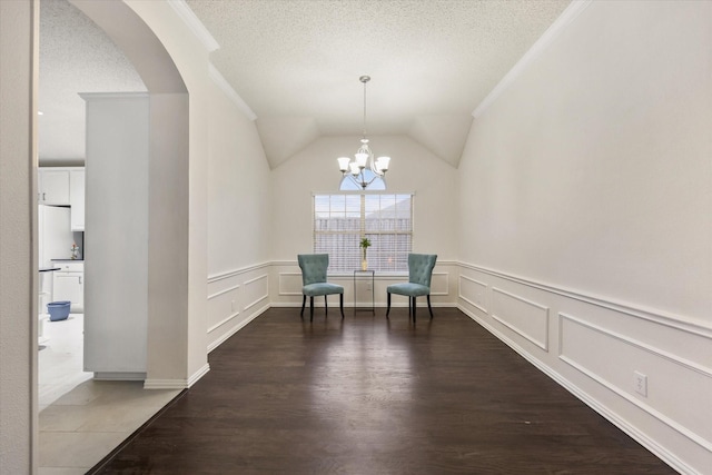 living area with a textured ceiling, lofted ceiling, wood finished floors, ornamental molding, and an inviting chandelier