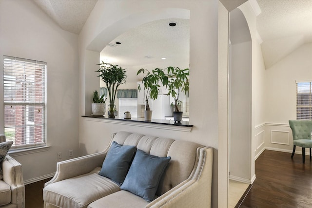 sitting room featuring arched walkways, vaulted ceiling, a textured ceiling, and wood finished floors