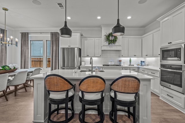 kitchen with stainless steel appliances, visible vents, ornamental molding, an island with sink, and wood finished floors